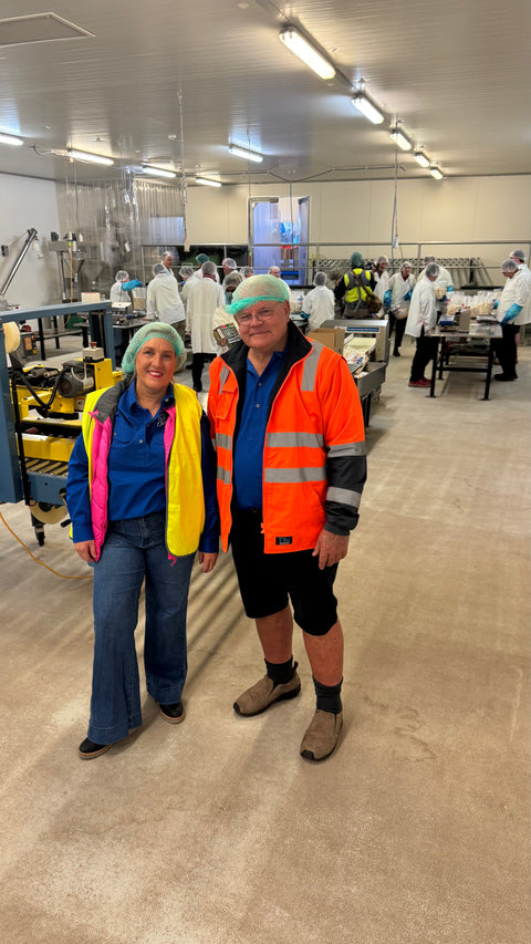 Two people in a factory setting wearing safety vests and hairnets